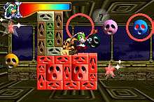A rainbow-colored spectrum in a futuristic gauge is in the upper-left area of the heads-up display. Marina, the main character, has green hear and wears white. She stands on a platform made of bricks, each brick is inlaid with an identical sad-looking face of different proportions. Floating balls with the same face float on the screen, as do rotating, neon-colored stars.
