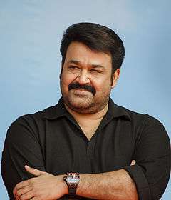 Mohanlal wearing a black T-shirt looking sideways with his hands crossed and a small smile in his face