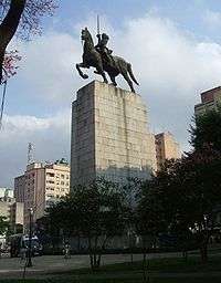 Photograph of a huge bronze statue atop a multi-story stone plinth depicting a mounted rider with upraised sword