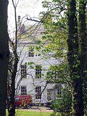 Photograph of the three-storey hall, painted white, framed by trees