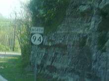 A shield for north Route 94 next to a rocky cliff