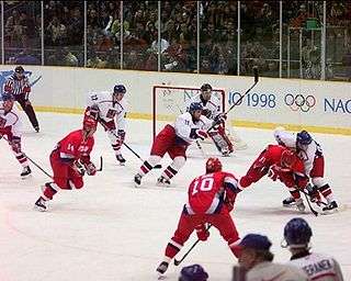 A hockey game between two teams; one is wearing red uniforms, and the other has white jerseys, red pants, and blue helmets.