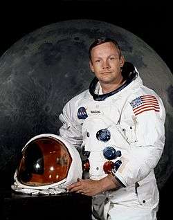 man in spacesuit holding helmet, large image of the moon in the background
