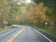 A highway cutting through a forest. Fall foliage is beginning to emerge.