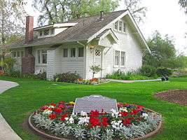 Photograph of the Richard M. Nixon Birthplace, a single-level, tree-shaded, white, wood-frame house.