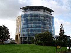 A semi-circular cylinder shaped tower building that is ten storeys tall, faced in glass and sandstone