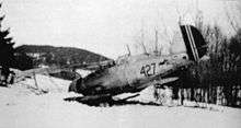 A black-and-white photo of a biplane sitting on the ground, shown in semi profile, viewed from the left-rear. The left wing and nose is buried in the ground. The aircraft is marked with the number 427.