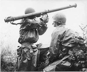 Two soldiers standing in brush, one aiming a bazooka