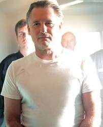 Oswald Danes, dressed in a plain white T-shirt, being accompanied from his prison cell