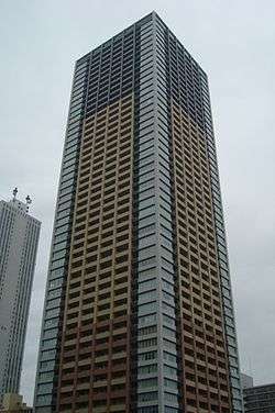 Ground-level view of a rectangular, window-dotted high-rise; the facades are tri-colored with white, beige and gray areas