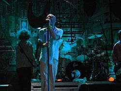 A color photograph of the band R.E.M. on stage
