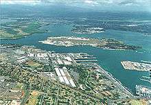 Aerial photograph of the Pearl Harbor Naval Base showing naval shore facilities in the foreground and Ford Island in the center.
