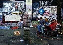 Photograph of people, graffiti-covered walls, and litter in Pigeon Park