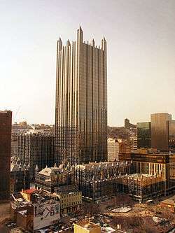  an all glass building with no other tall buildings around it. It is topped off by a glass spire on each corner and is surrounded by much shorter but similarly Gothic glass buildings.