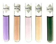 Five fluids in glass test tubes: violet, Pu(III); dark brown, Pu(IV)HClO4; light purple, Pu(V); light brown, Pu(VI); dark green, Pu(VII)