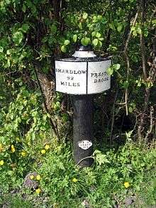 A black post supports a plaque which says on the left "Shardlow 92 miles" and on the right "Preston Brook".