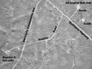  Black and white aerial view of several roads through a forest with a few buildings. The image is labeled "Jet engine test cells" in the upper right corner with buildings in two cleared circles at end of small roads labeled "North" and "South". In the lower left corner is a larger building in a cleared area labeled "Reactor & hot cells". The road to this is labeled "Reactor Road" and it leads to the labeled "Quehanna Highway". A clearcut strip is labeled "Electricity transmission line".