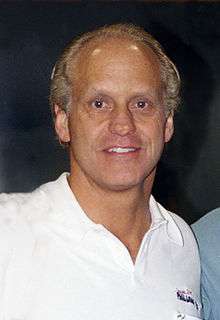 A man wearing a white polo looks straight ahead.