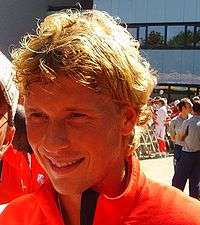 A close-up photograph of a smiling blonde man wearing a red sport sweater.
