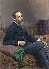A man with glasses and a long beard sitting on a sofa, smoking