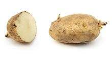 A sliced and a whole potato side by side, both dark brown with sprouts emerging.