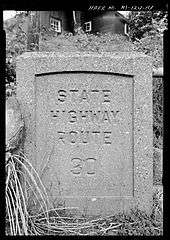 An old stamped bridge made and indented of stone off the side of the highway with the stamp reading State Highway Route 30