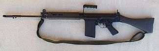 A black FN FAL battle rifle lain on a grey background, pointing to the viewer's left