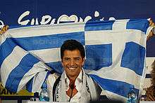 Smiling man, raising a blue-and-white Greek flag