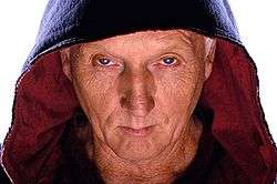 A close-up of Tobin Bell as The Jigsaw Killer wearing his signature black hooded robe with red lining.