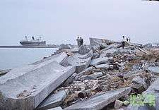 Slightly elevated photo showing a pile of debris near the coast, with some onlookers nearby.