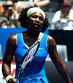 A black woman with a blue dress holding a tennis racket out in front of her
