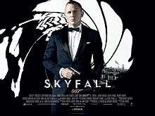 The poster shows James Bond wearing a tuxedo and holding a gun, standing in front of an image that looks like it was taken from the inside of a gun barrel, with the London skyline visible behind him. Text at the bottom of the poster reveals the film title and credits.