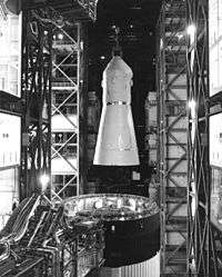 Black-and-white picture from inside a tall building with a space capsule being lifted from the top of a rocket