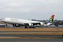 An Airbus A340-600 in the current livery. It is landing on a runway, facing left.