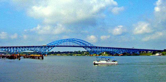 Profile of South Grand Island Bridge. Two sky-blue steel spans cross the river in five arches. The central arch alone is above the roadway, permitting passage of large freight ships.