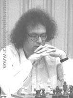 black and white photograph of dark-haired male wearing glasses, seated at chess game