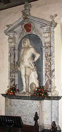 White statue of man with long hair or wig as part of an elaborate stone wall memorial