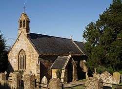 Stone building with arched window and slate roof. In the foreground are gravestones.