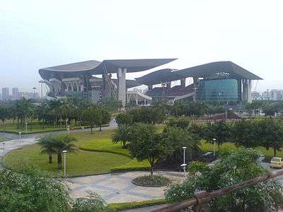 A far view of a stadium, with two large sitting pavilions and greenery around the compound.