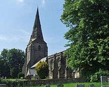 A stone church seen from the southeast, with a broach spire at the west end