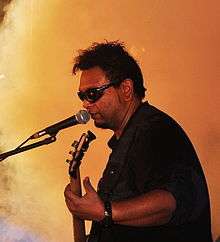 Man in dark glasses onstage, playing guitar and singing