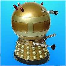 A squat Dalek, painted overall in gold. It has brass-coloured hemispheres, collars and two wide bands around the spherical head section, the upper rear portion of which is adorned with seven red lights.