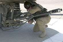 Soldier adjusting big gun hanging from helicopter