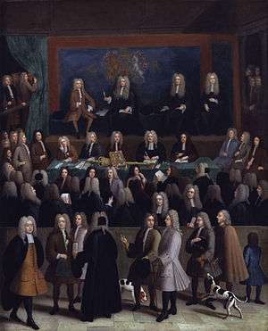 A rectangle picture of a courtroom.  Dozens of men in a courtroom in 1750s era court suits and wigs.  A blue wall at the back contains a coat of arms.  On a raised stage at the back are four men.  Several onlookers, some with dogs and children, pass by on a sidewalk looking in on the court proceedings.