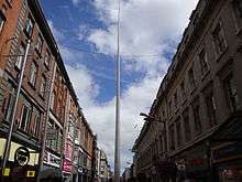 Tall pole rising high into the sky above buildings lining a city centre shopping street