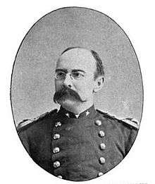 Head and shoulders of a balding white man with a drooping handlebar mustache and pince-nez glasses. He is wearing a double-breasted military jacket with shoulderboards.