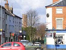 The corner of a street with a public house called The Ivy Bush on the right side. In the background two tall brick towers can be seen further left.