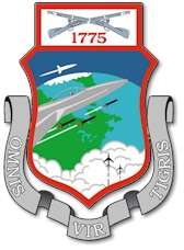A shield ringed in red encases a view of the Northeastern United States. Jets are visible against the background. The wing's motto is shown around the shield.
