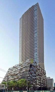 Ground-level view of a rectangular, brown high-rise; it sits on a larger base that has multi-colored panels
