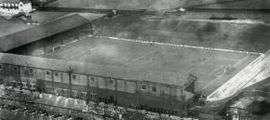 Bird's eye view of a football stadium with a grass pitch. Two sides of the ground have covered stands while the other two have uncovered terracing.